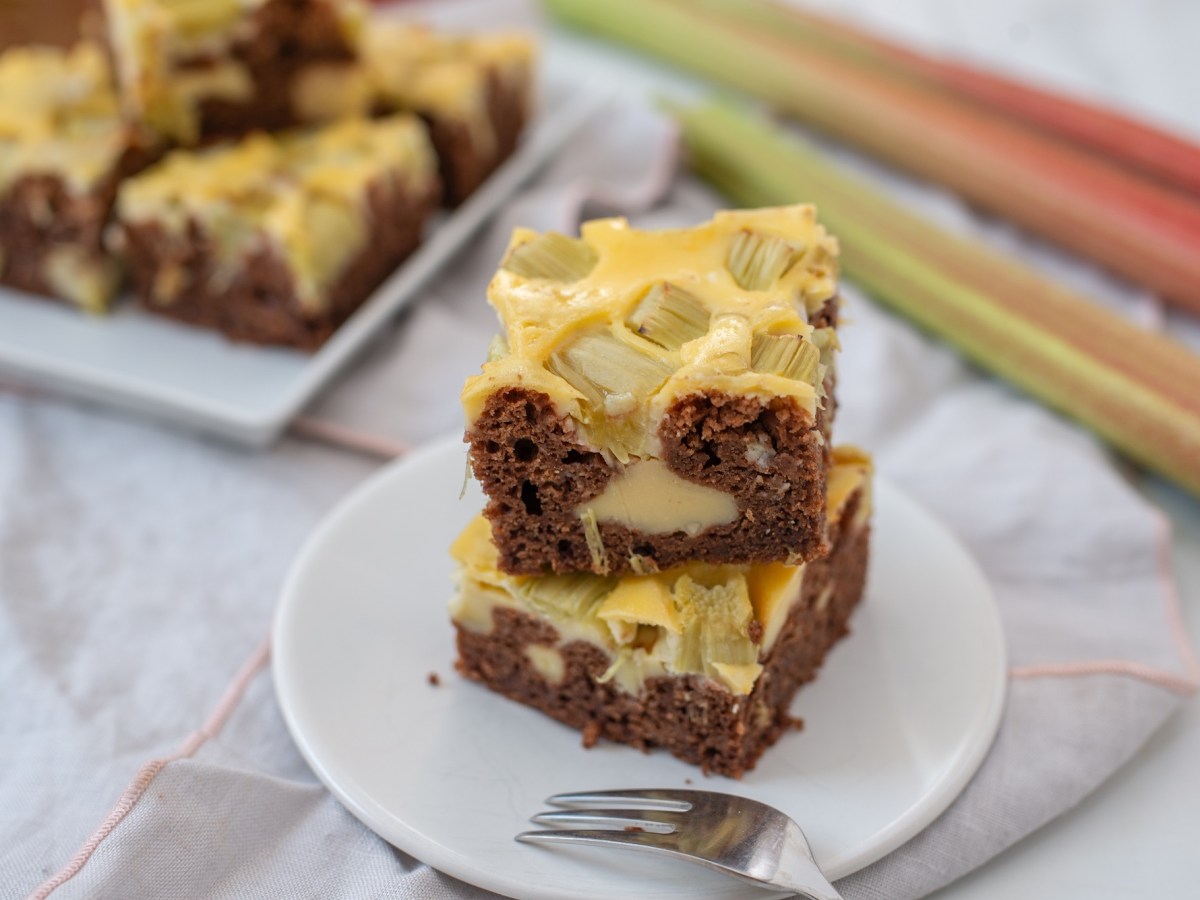 Teller mit Rhabarber-Cheesecake-Brownies, Gabel und Rhabarberstangen