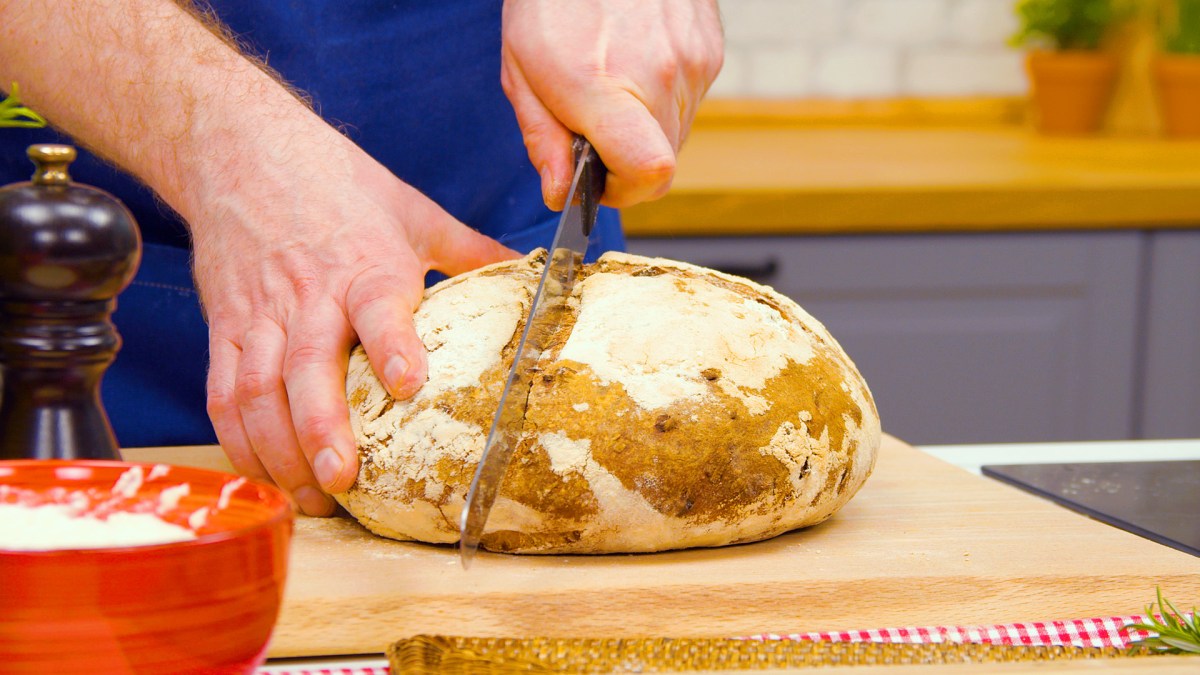 Sauerteigbrot backen: jemand schneidet ein Sauerteigbrot mit dem Messer durch.