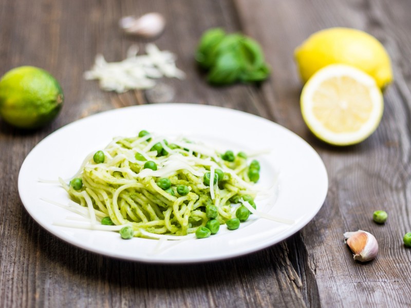 Ein teller Spaghetti e piselli mit Zitrone und Knoblauch daneben.