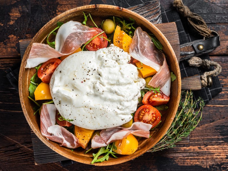 Tomatensalat mit Burrata und Schinken in einer Schüssel.