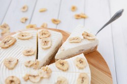 Bananen-Mascarpone-Torte auf einem Holzbrett. Mit einem Kuchenheber wird ein Stück entnommen.