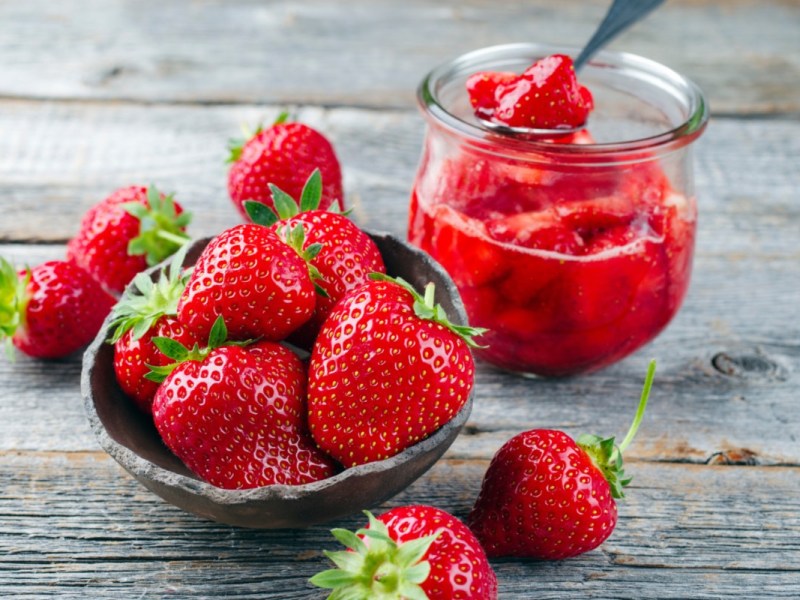 Ein Glas Erdbeerkompott, daneben frische Erdbeeren.