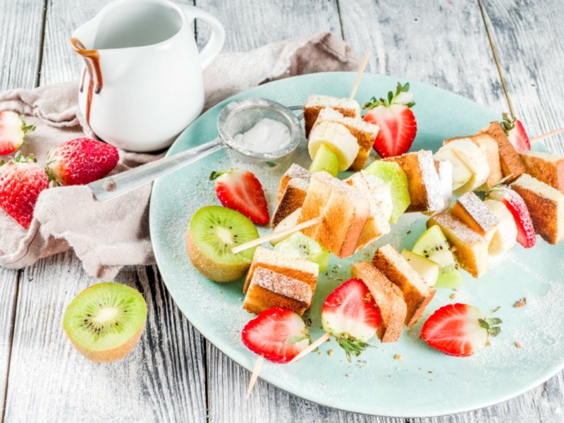 Mehrere French Toasts am Spieß mit Erdbeeren und Kiwis auf einem Teller.