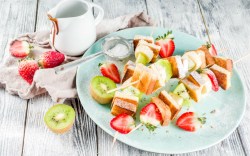 Mehrere French Toasts am Spieß mit Erdbeeren und Kiwis auf einem Teller.