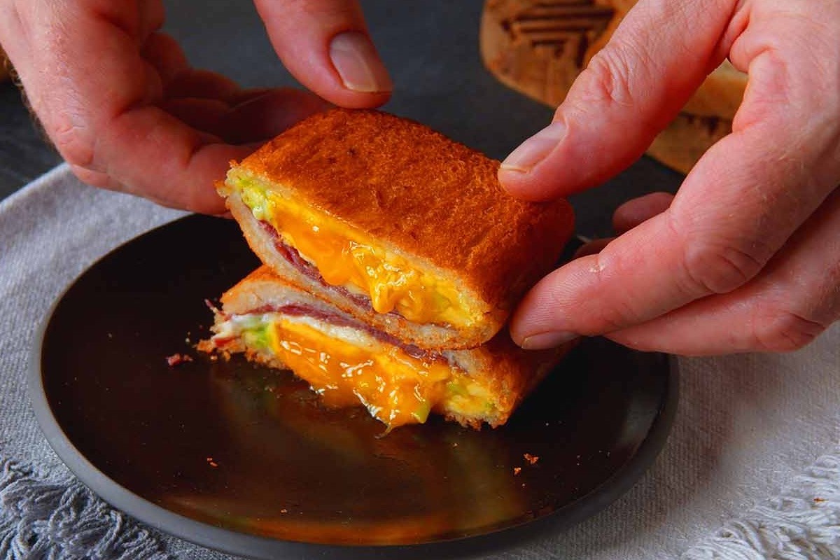 Ein gebackenes Sandwich auf einem Teller, das halbiert wurde und von zwei HÃ¤nden gehalten wird.