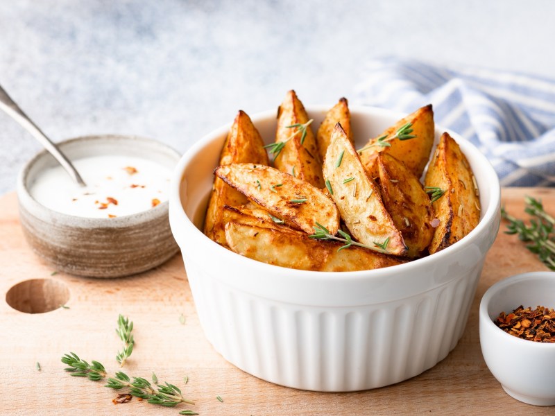 Eine weiße Schale Kohlrabi-Wedges auf einem Brett, auf dem auch einige weitere Schüsseln mit Dips stehen.