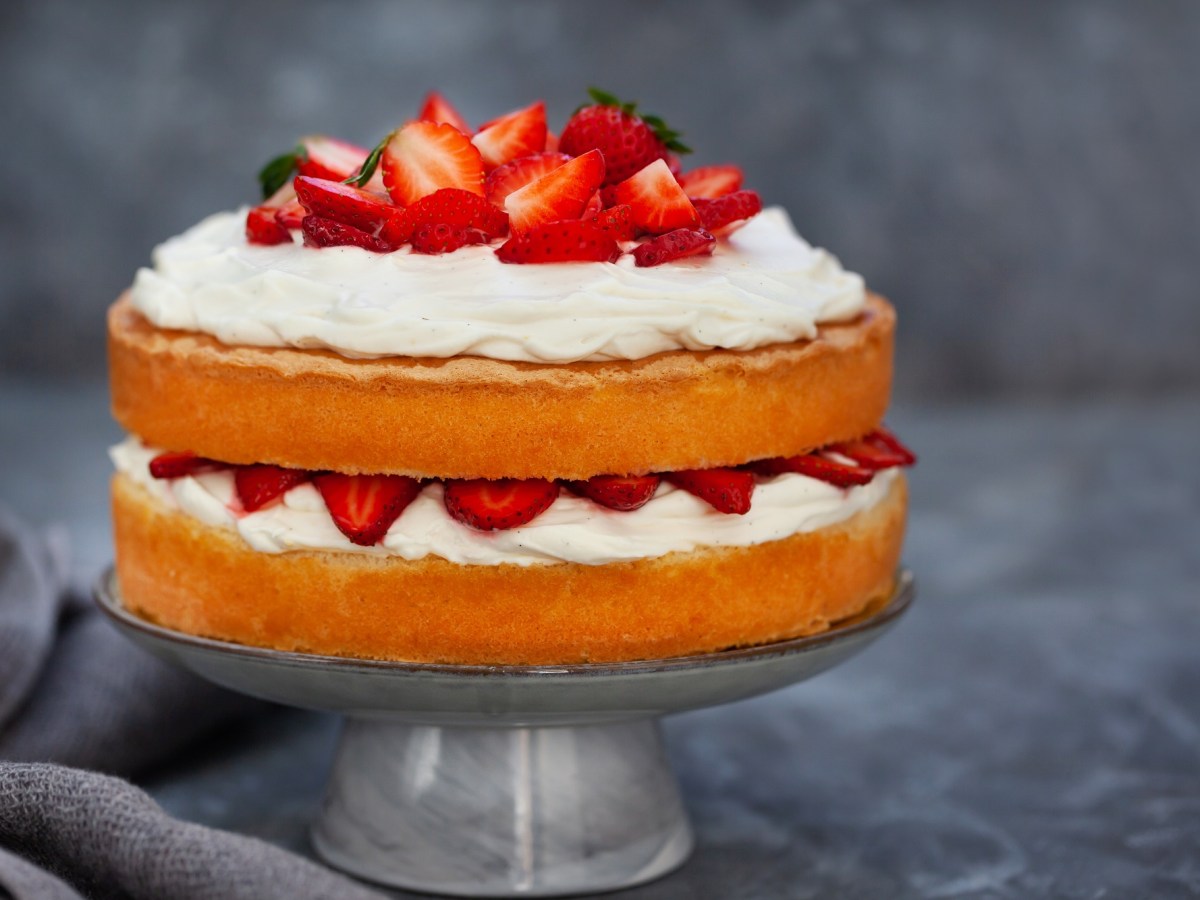 Ein TortenstÃ¤nder mit Naked Cake mit Erdbeeren auf zwei TortenbÃ¶den und Sahne.