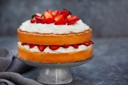 Ein Tortenständer mit Naked Cake mit Erdbeeren auf zwei Tortenböden und Sahne.