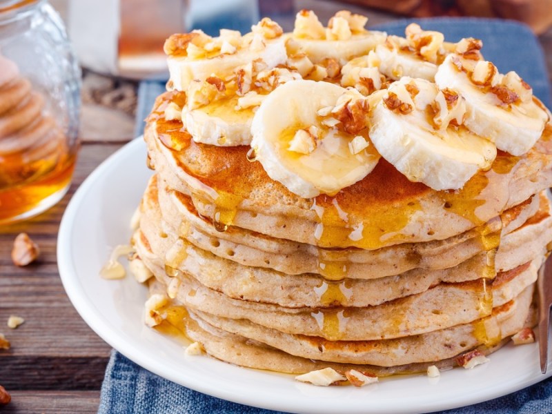 Pancakes auf einem weißen Teller mit Banane, Walnüssen und Sirup