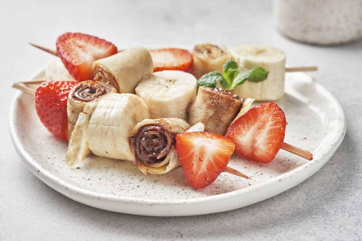 3 Pfannkuchen-Spieße mit Erdbeeren und Bananen auf einem Teller.