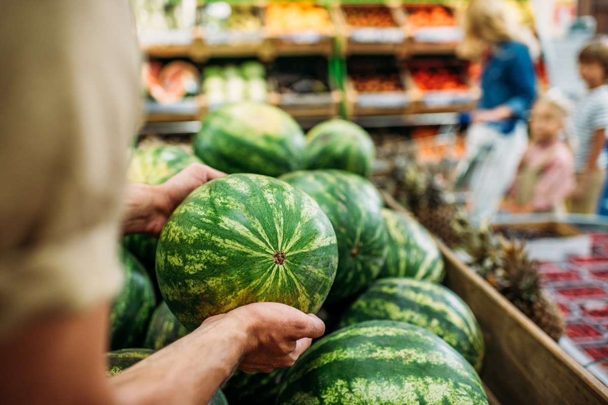 Eine Frau nimmt eine reife Melone aus einem Haufen Wassermelonen im Supermarkt heraus.