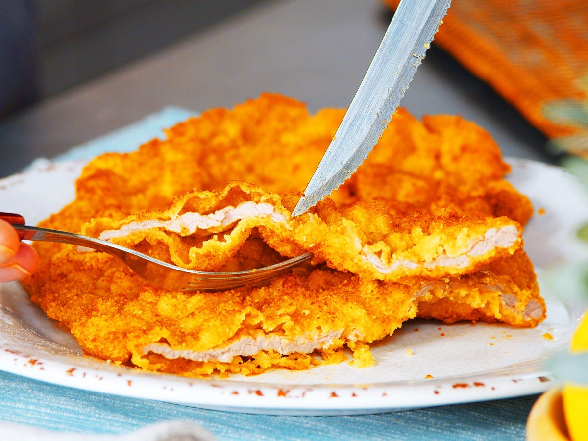 Rezept für Wiener Schnitzel: ein Wiener Schnitzel mit Kalb auf einem Teller, das angeschnitten wird.