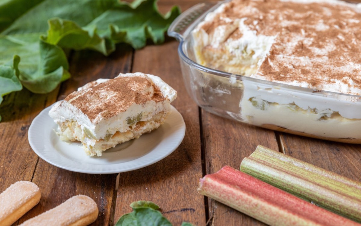 Eine Portion Rhabarber-Tiramisu auf einem Teller. Das restliche Dessert steht in einer Auflaufform dahinter.