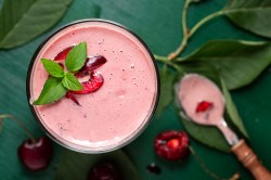 Sauerkirsch-Smoothie mit Minzblatt und Löffel daneben.