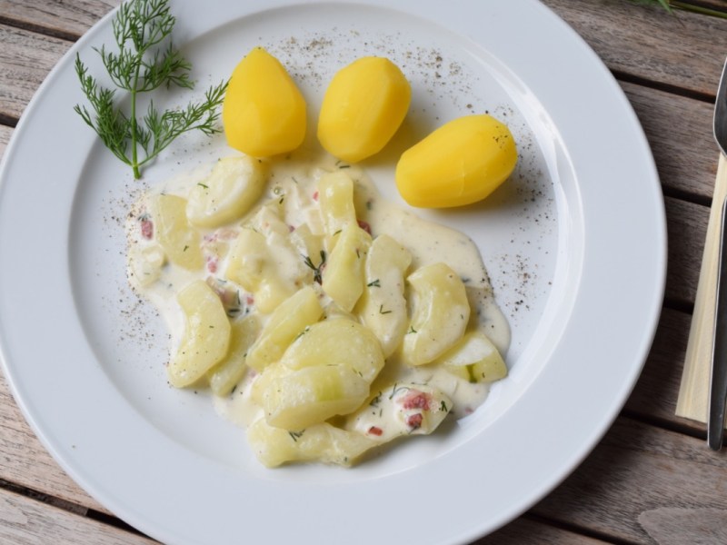 Rezept für Schmorgurken: Ein Teller mit Schmorgurken und Kartoffeln. Daneben liegt Besteck.