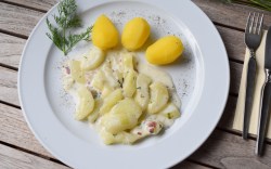 Rezept für Schmorgurken: Ein Teller mit Schmorgurken und Kartoffeln. Daneben liegt Besteck.