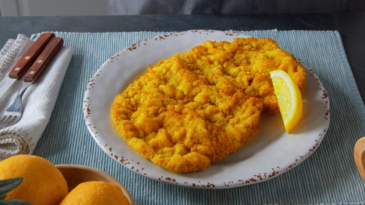 Schnitzel selbst machen: ein paniertes Schnitzel auf einem Teller, daneben Messer und Gabel.