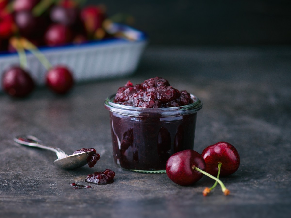 Ein Glas mit Schwarzwälder Kirschmarmelade und Kirschen auf dem Tisch