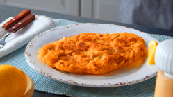 Schweineschnitzel auf einem weißen Teller. Daneben liegt eine Zitronenspalte.