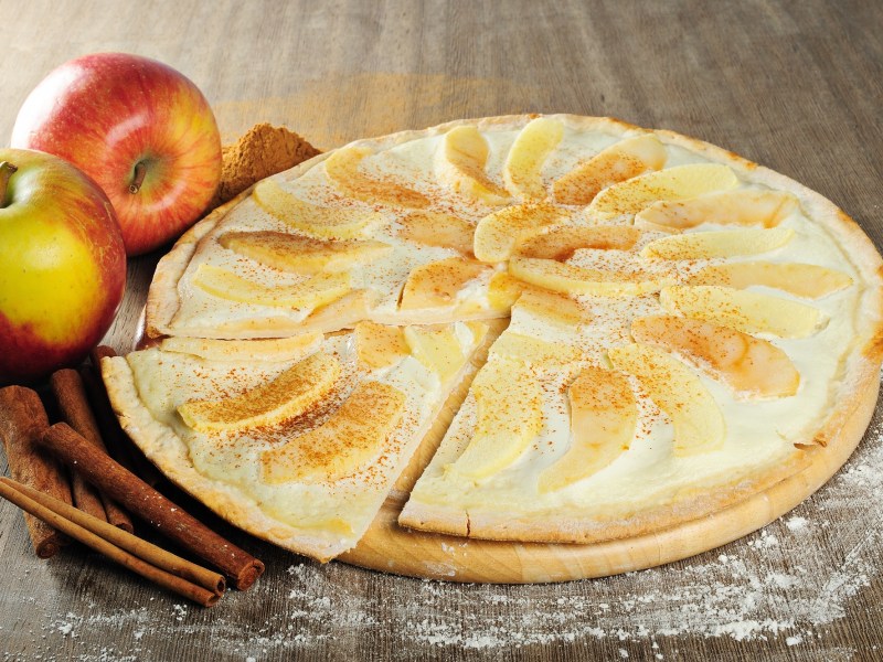 Apfel-Flammkuchen auf einem Tisch, Äpfel und Zimt daneben