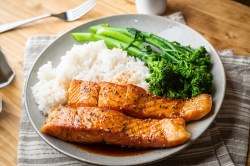 Teriyaki-Lachs mit Reis und Brokkoli serviert auf einem weißen Teller.