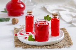 3 Flaschen Wassermelonen-Sirup auf einem weißen Teller, garniert mit Minze, im Hintergrund eine weitere Flasche.