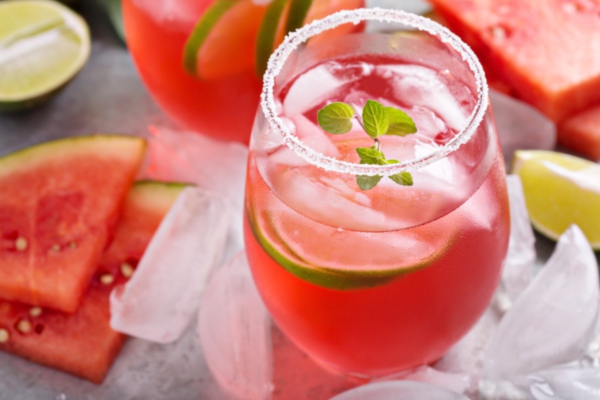 Ein Glas Watermelon Man. Drumherum liegen Limetten, Eiswürfel und frische Wassermelone.