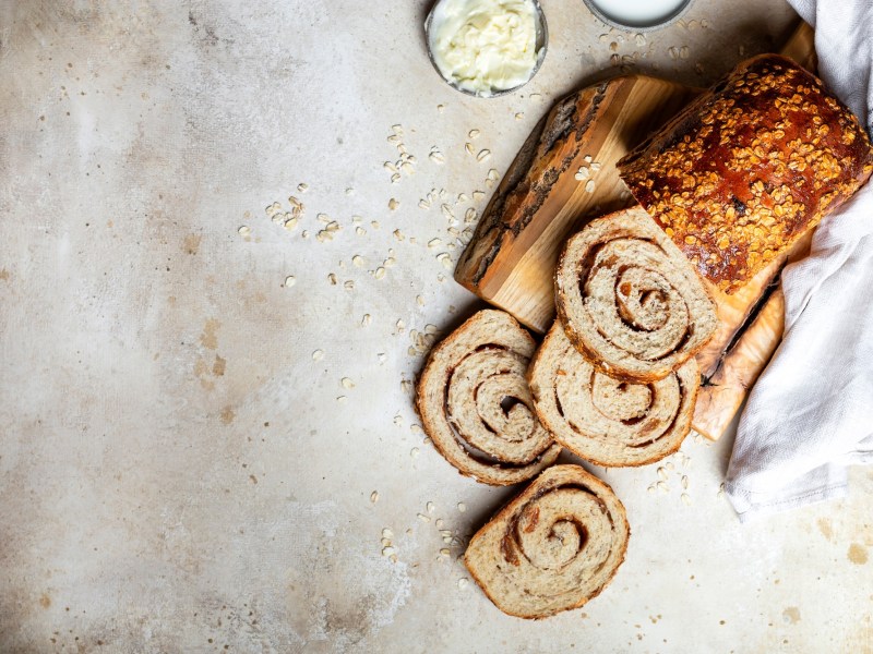 Zimtschnecken-Brot, von dem schon einige Scheiben abgeschnitten sind, auf einem Holzbrett.