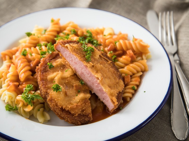 DDR-Rezepte: Jägerschnitel mit Spirellinudeln und Tomatensoße auf einem Teller, daneben Messer und Gabel, Nahaufnahme.