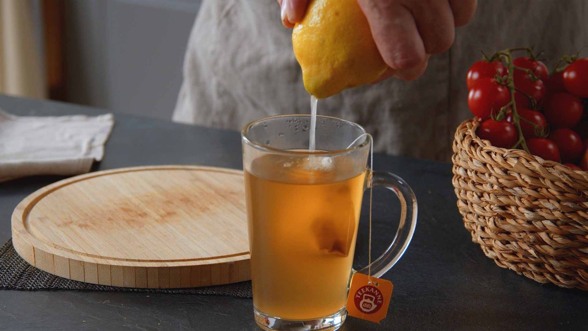 Food-Hacks: eine Hand presst eine Zitrone in einen Becher Tee.