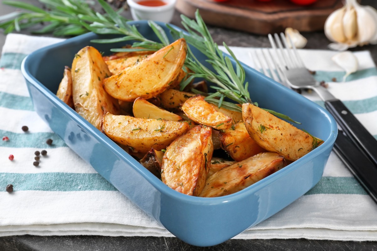 Eine Auflaufform mit Kartoffelspalten mit Knoblauch und Rosmarin auf einem blau-weiß gestreiften Geschirrtuch.