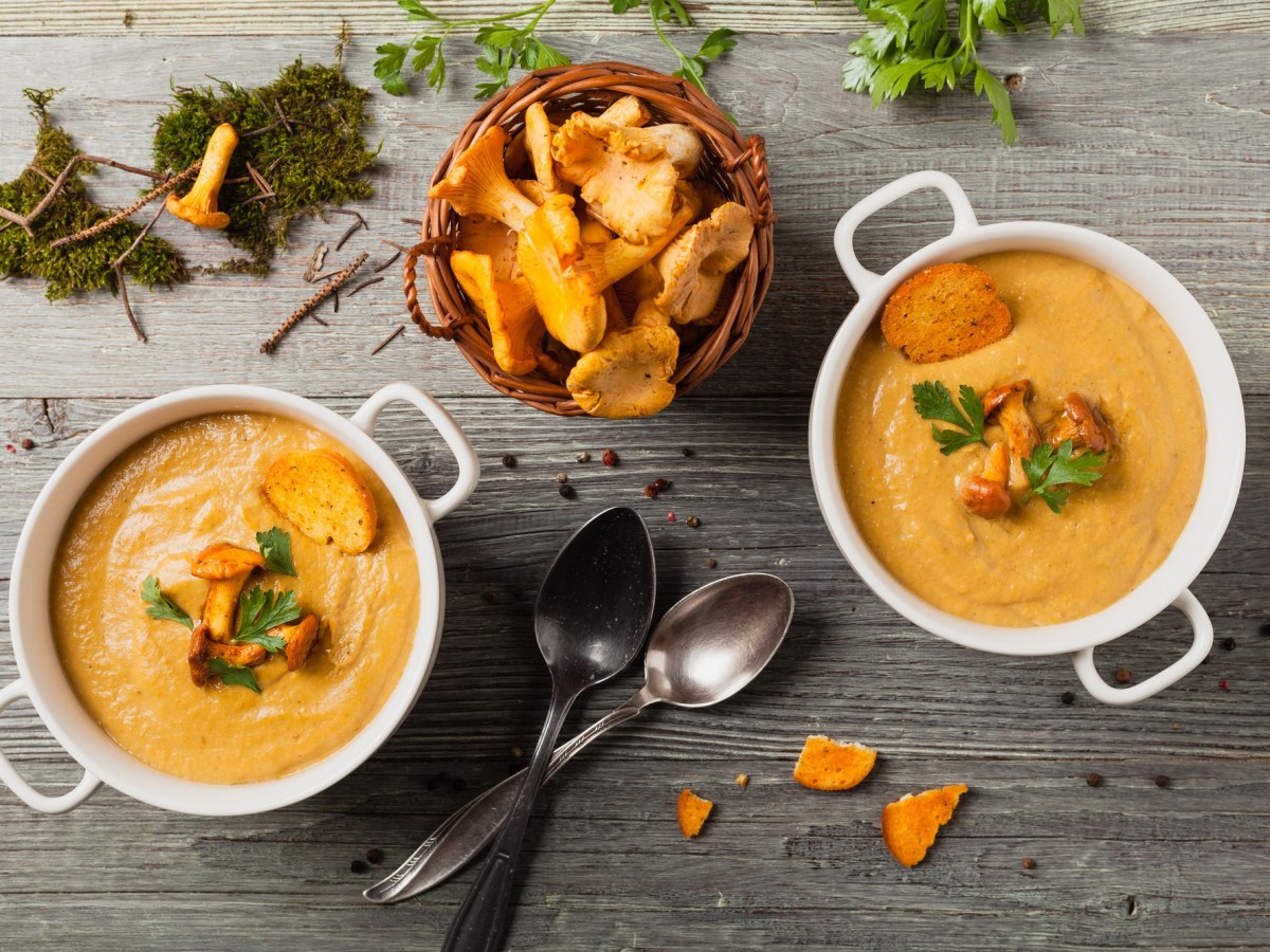 Zwei Schüsseln mit Pfifferlingcremesuppe und einer Schale Pfifferlingen.