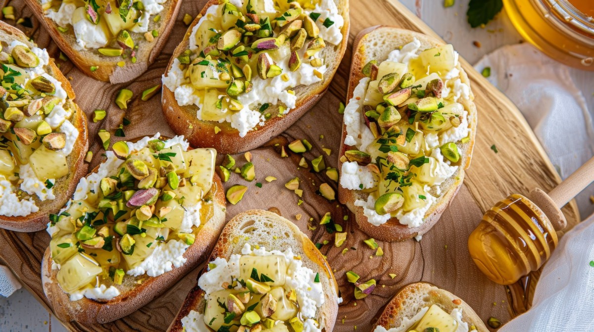 Brett mit Ricotta-Pistazien-Toasts und Honiglöffel daneben