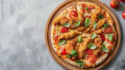 Schnitzelpizza auf grauem Tisch.