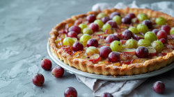 Stachelbeer-Tarte auf einem Kuchentablett. Drum herum liegen weitere Stachelbeeren.