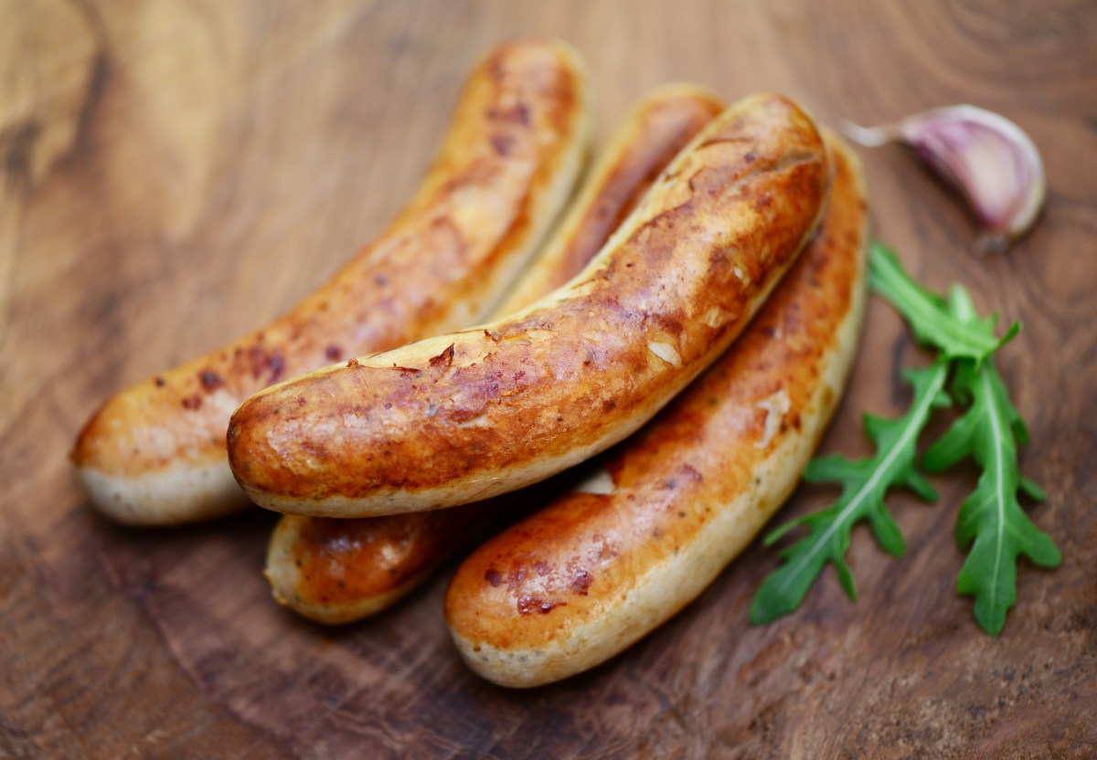 Thüringer Rostbratwurst: Mehrere Würste auf einem Holzbrett. Daneben Rucola und Knoblauch