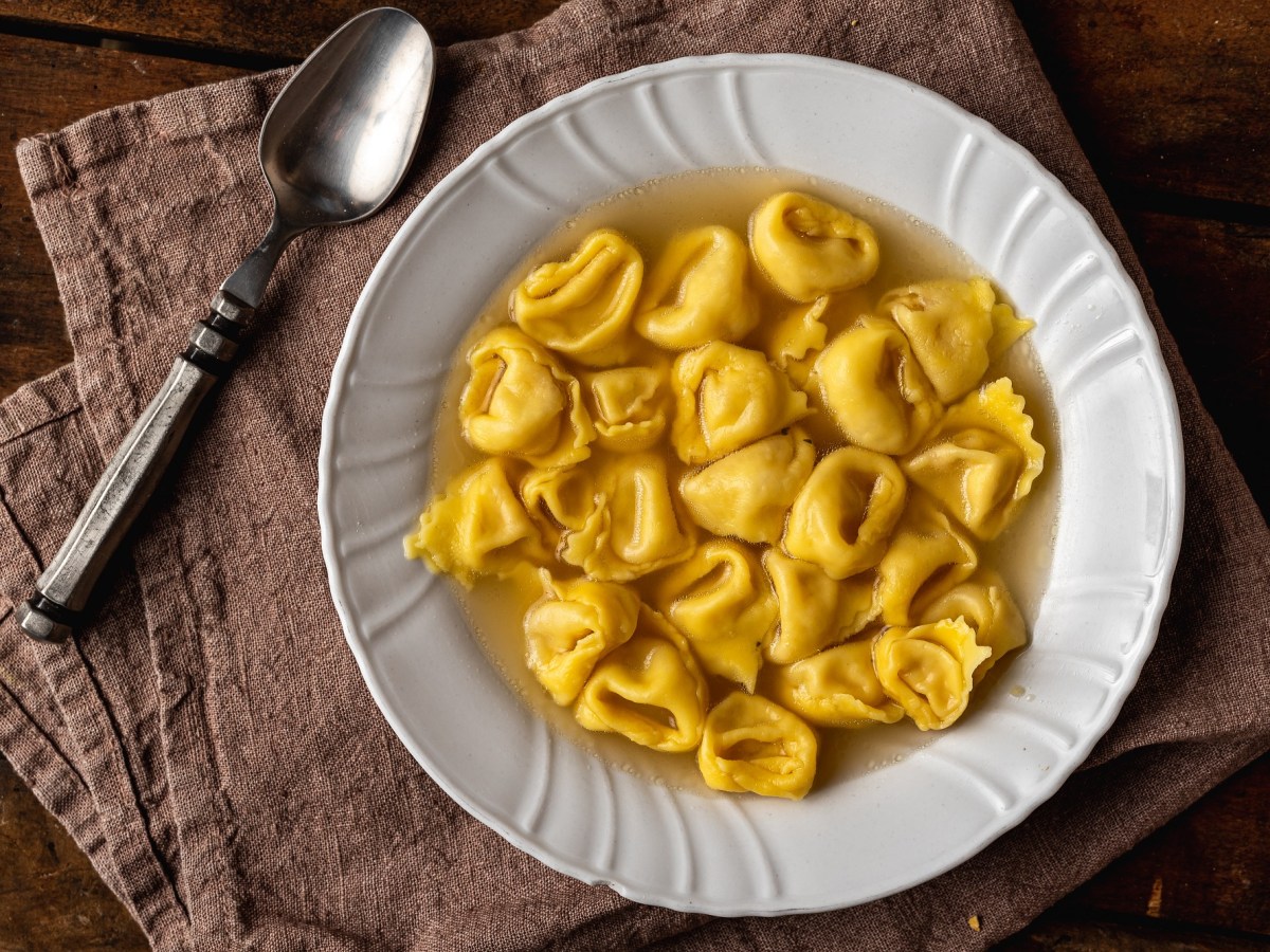 Tortellini in Brodo in einem weißen Teller. Daneben liegt ein Löffel.