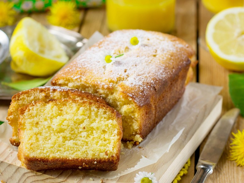 Ein angeschnittener Zitronenkuchen mit Kamille auf einem dekorierten Tisch.