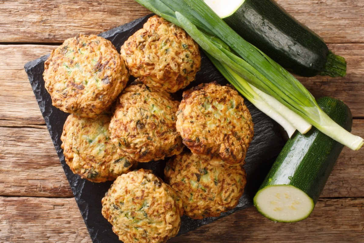 Mehrere Zucchini-Bällchen in der Draufsicht. Daneben liegen Zucchini und Frühlingszwiebeln.