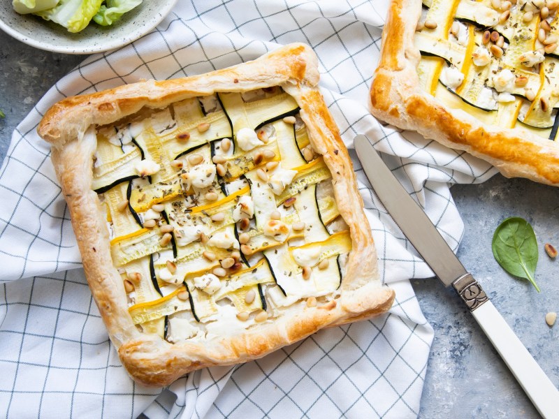 Zwei Zucchini-Blätterteig-Tartes auf kariertem Tischtuch