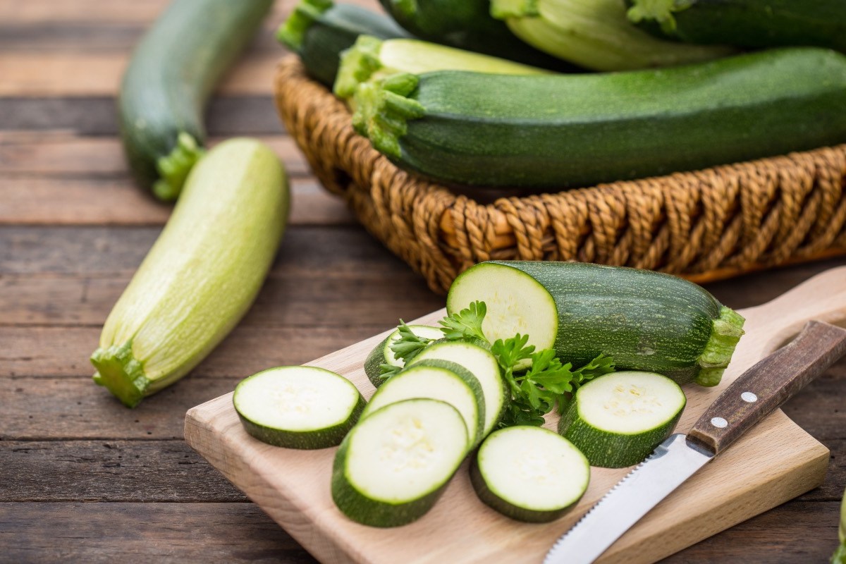 Aufgeschnittene Zucchini auf einem Brett. Im Hintergrund Zucchini in einem Korb.