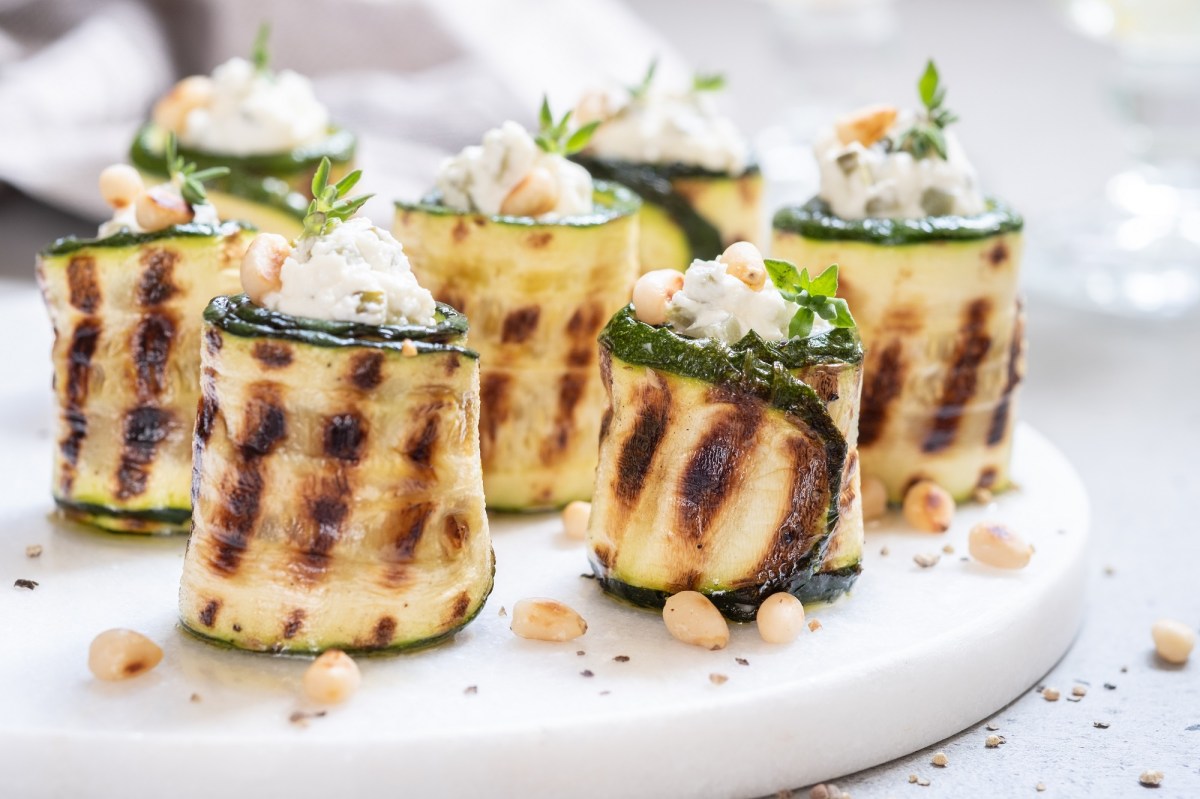 Zucchini-Röllchen mit Frischkäse auf einem Tablett.