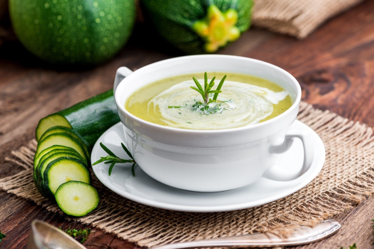 Eine Schüssel mit Zucchini-Suppe. Daneben liegt eine aufgeschnittene Zucchini.