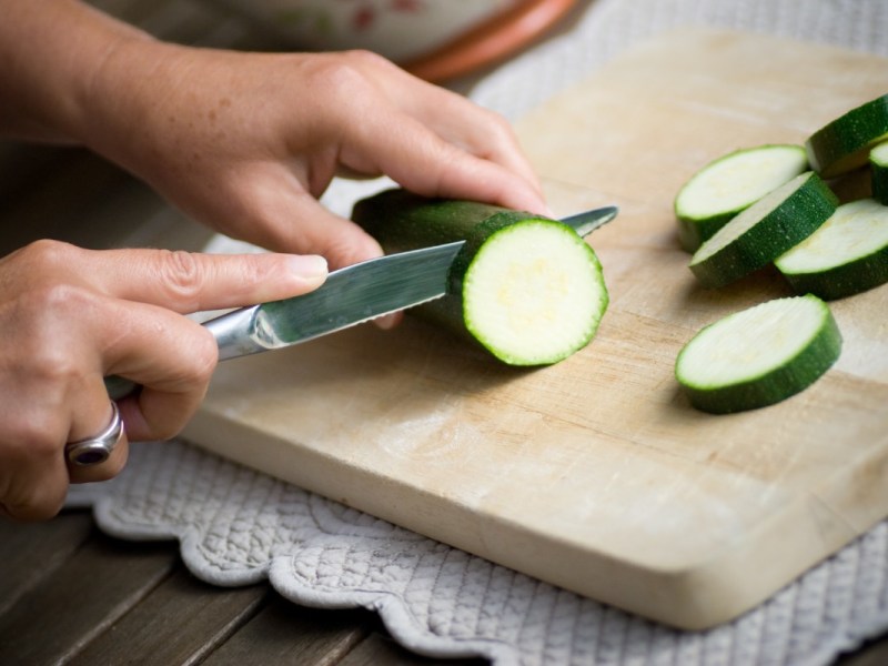 Zucchini zubereiten: Eine Zucchini wird auf einem Holzbrett in Scheiben geschitten.