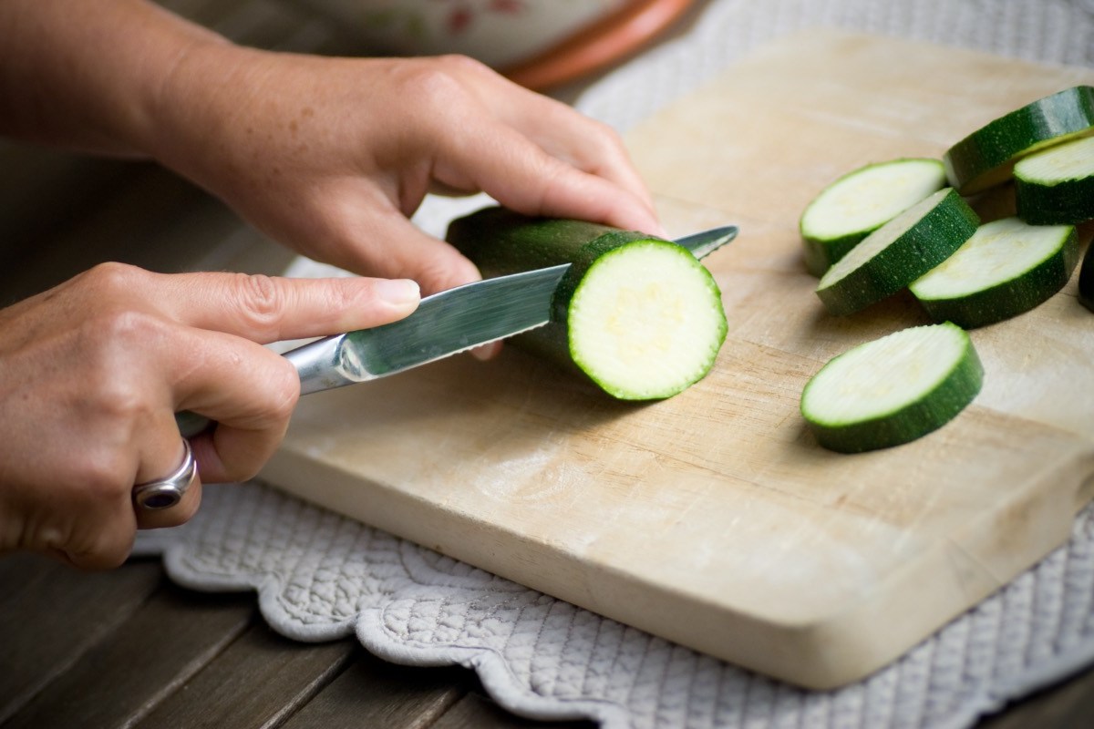 Zucchini zubereiten: Eine Zucchini wird auf einem Holzbrett in Scheiben geschitten.