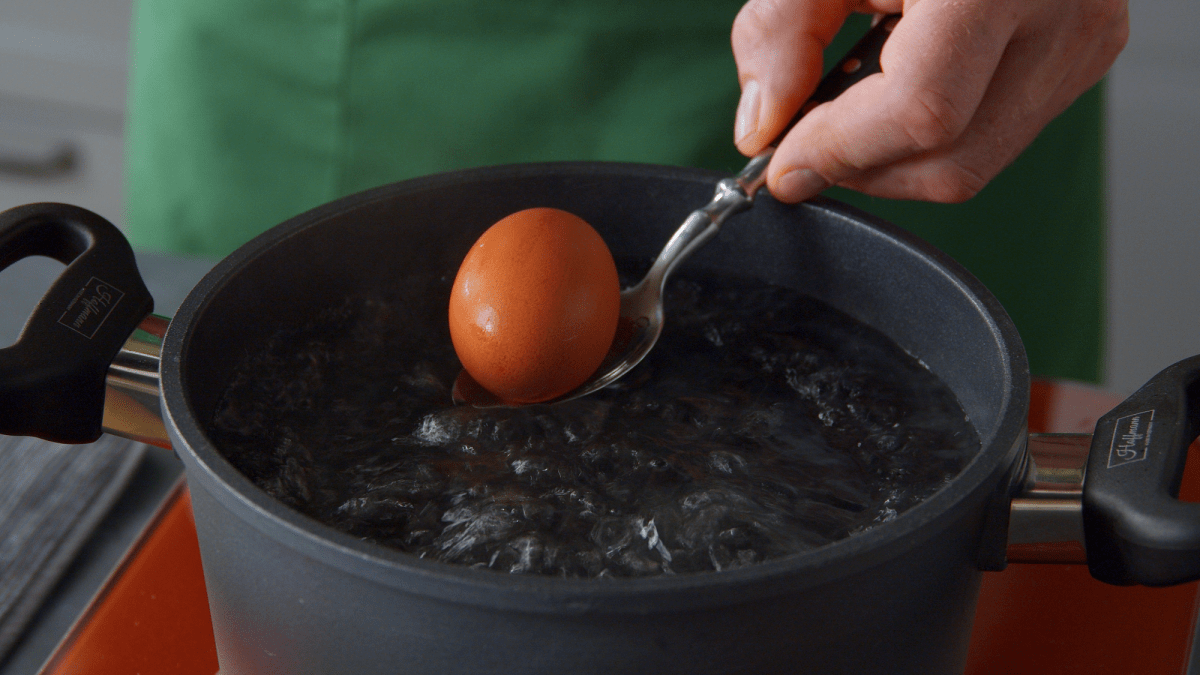 Eier kochen: Eine Hand gibt ein Ei in kochendes Wasser.