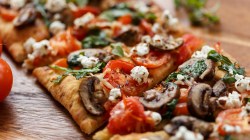 In Stücke geschnittene Fladenbrot-Pizza mit Pilzen, Feta und Tomaten.