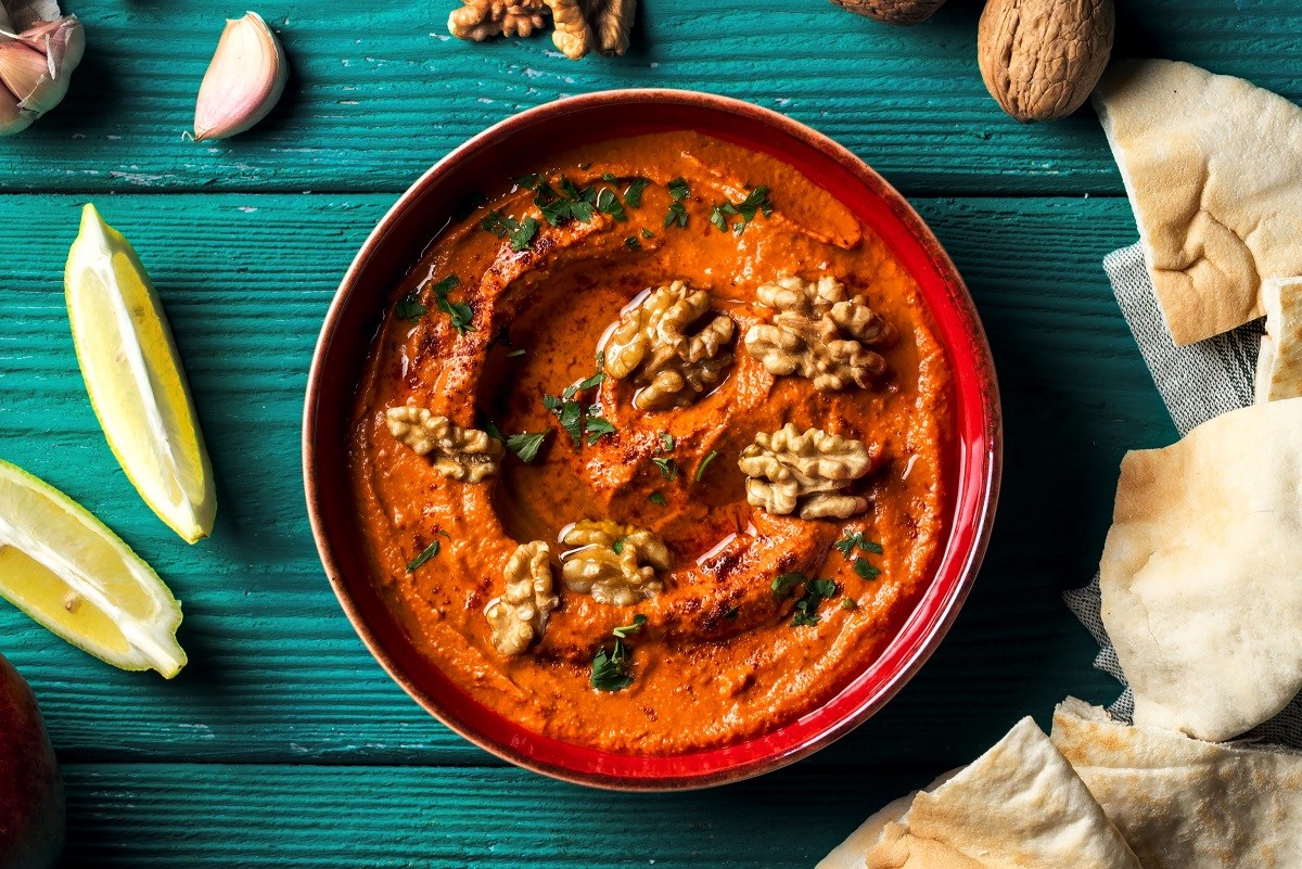 Schale Granatapfel-Paprika-Dip mit Fladenbrot Zitrone und Gewürze daneben.