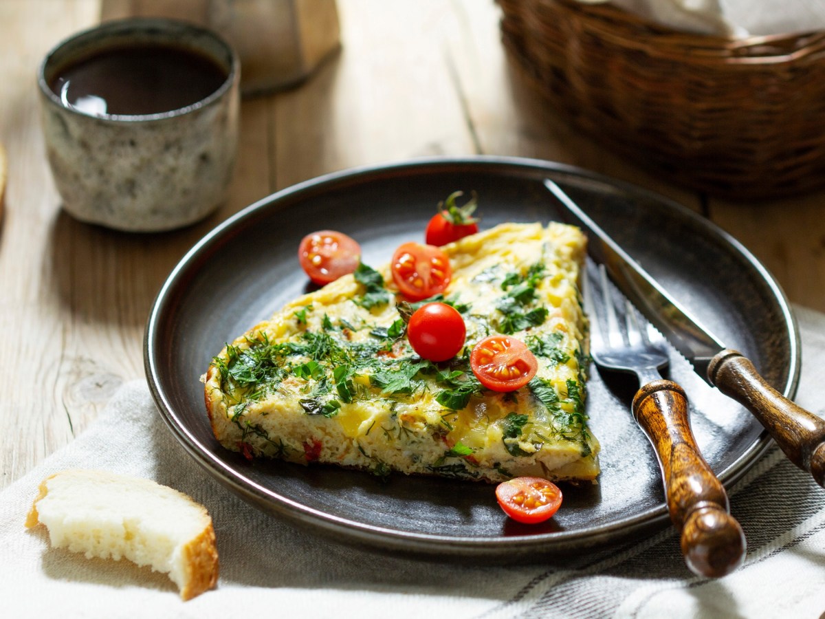 Ein Teller mit einem Stück Mangold-Feta-Frittata garniert mit Tomaten, daneben Messer und Gabel.