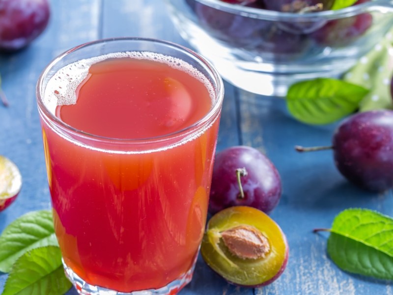 Ein Glas selbst gemachter Pflaumensaft. Drumherum liegen frische Pflaumen.